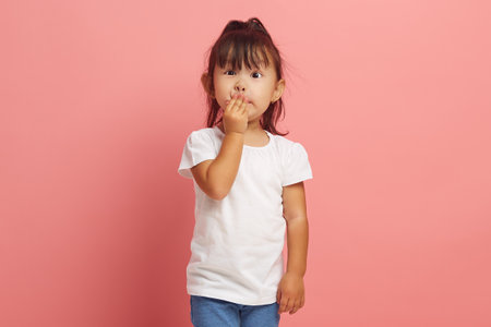 Little Asian girl covers her mouth with her hand with her eyes wide open, expresses embarrassment...