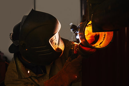 Worker in safety mask welds metal at industrial enterprises.