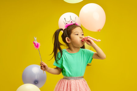Birthday Princess Blowing Party Whistle with Balloons Against Yellow Isolatedの写真素材