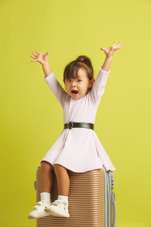 Little joyful girl sits on suitcase and cheerfully spreads her arms to up, expressing happiness from a long-awaited vacation and trip to the seaの写真素材