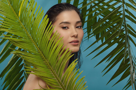 Well groomed woman peeks out from behind palm leaves.