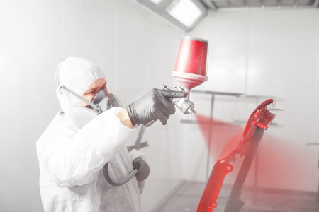 Male worker painting a fender of car in a white paint booth.の写真素材