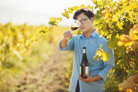 Male Sommelier Holding Glass of Red Wine Standing in Vineyard
