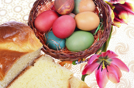 Easter cakes, colored eggs in wicker basket  and tulips on   knitted cover