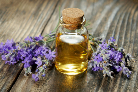 A bottle of essential oil with fresh lavender twigs on a wooden background ,selective focus.の写真素材