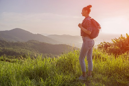 Hipster young girl with backpack enjoying sunset on peak of foggy mountain. Tourist traveler on background view mockup. Tonedの写真素材