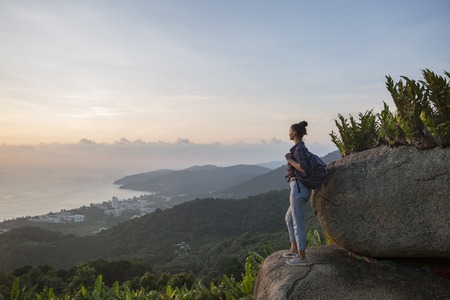 Hipster young girl with backpack enjoying sunset on peak mountain. Tourist traveler on background valley landscape view mockup.の写真素材