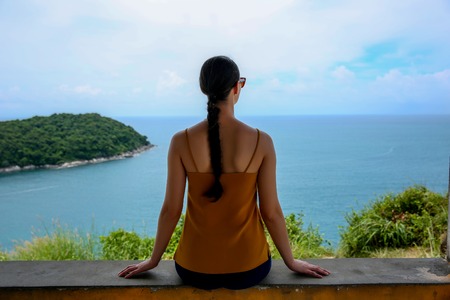 Young woman sitting and relaxing on a natural coastal rock, contemplating the sea against a sky. Well being healthy lifestyleの写真素材