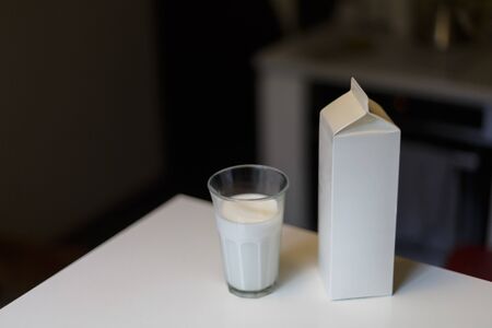 Carton box and glass of milk on table in kitchenの写真素材