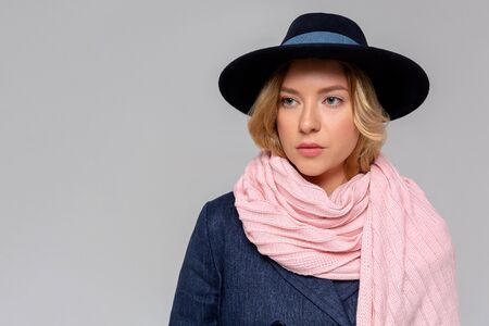 Fashionable woman in blue coat, pink scarf and black hat posing in studio, looking at camera. cold season. Autumn, Spring or winter look.の写真素材