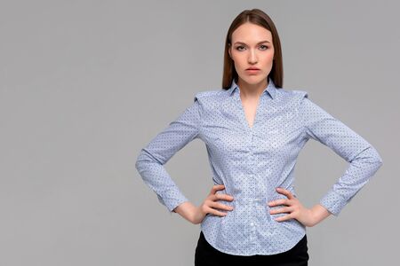 Beautiful smiling young woman is holding hands on hip and looking at camera. Three quarter length studio shot on monochromatic background.の写真素材