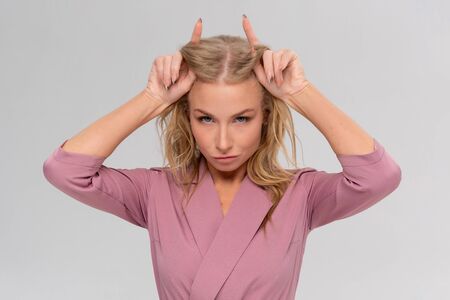 Rebellious charming woman showing inner devil having fun stubborn, smiling broadly playing holding index fingers behind head imitating horns, squinting happily, laughing out loud gray backgroundの写真素材