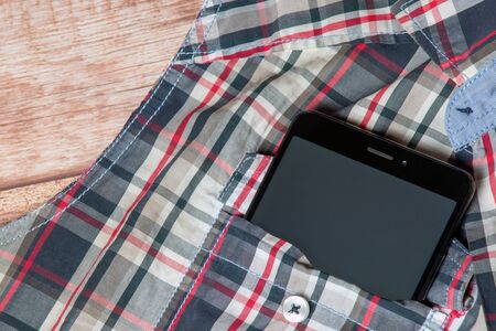 black smartphone sticking out of a sleeveless shirt pocketの写真素材