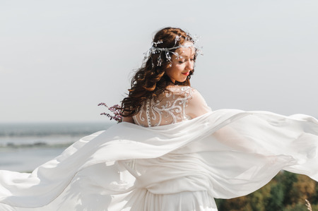 The bride in a white dress with a beautiful bouquet of fresh flowers, standing on a hill with views of the river flood.の写真素材