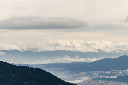 Winter in the mountains, dense clouds lay over the tops of mountains and roofs of houses, snow lies on the tops and roofs of wooden housesの写真素材