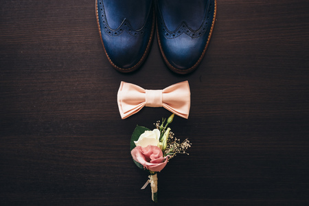 Stylish men's shoes on a dark wooden table next to the shoes is a pink butterfly, a boutonniere with live roses and a mechanical clock, the groom is ready for the weddingの写真素材