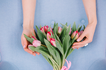 The girl hugs her bouquet with a pink ribbon - tender pink pion-shaped tulips on a blue backgroundの写真素材