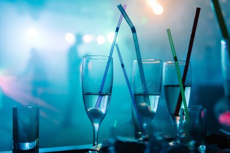 A noisy party in a nightclub with light music, on the table are stacks and glasses with champagne with stuck multi-colored strawsの写真素材