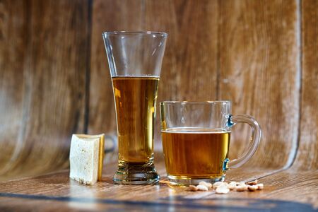 A glass and a mug of tasty beer stand on a brown background with cheese and nuts. Fragrant beer lit by beautiful light stimulates appetite.の写真素材