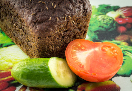 Loaf of bread, cucumber and tomato on a cutting boardの写真素材
