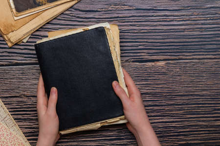 Vintage black notepad with old paper sheets in both hands and copy space in the right on wooden...