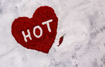 Word "hot" written on red chilli powder with chilli pod on concrete background. Spicy food concept.の写真素材