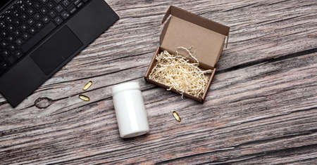 Mock up of white bottle with omega vitamin pills, laptop and cardboard box on wooden backgroundの写真素材