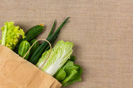 Fresh green vegetables in paper bag on burlap background and copy space. Delivery healthy food,...