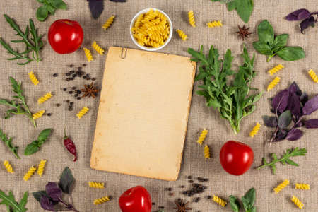 Old vintage paper sheet with empty space for text and fresh herbs, spices and pasta on coarse linen...