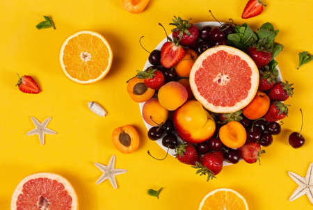 Plate full of ripe fruits and berries with seashell and starfish on bright  yellow backgroundの写真素材