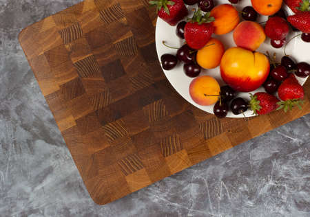 Fruits on the plate with wooden cutting board on background, top viewの写真素材