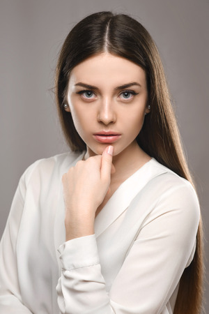 Beauty portrait young girl sitting at the white table in white blouse and black skirt on gray background in bussiness styleの写真素材