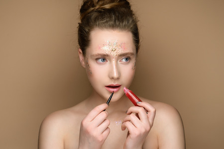 Portrait of young beautiful girl with pink lipstick in hands on the gold background. Nude makeup with tinsel and updo. Concept of the beauty.の写真素材