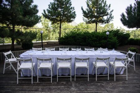 White served table with many chairs outdoor on background of green treesの写真素材
