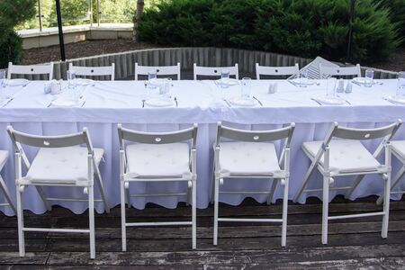 White served table with many chairs outdoor on background of green treesの写真素材