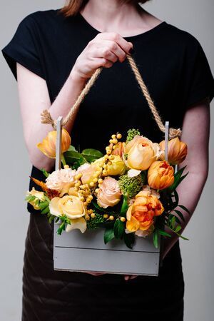 Bouquet of flowers in a wooden box in the hands of a woman florist. Rosa spray Catalina, ilex, skimmia, carnation, eustoma, tulipの写真素材