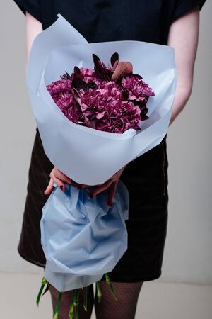 Bouquet of flowers in blue transparent package in the hands of a woman florist. Carnation, cotinusの写真素材