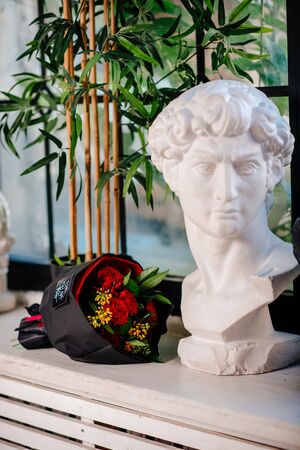 Bouquet of flowers in black package and plaster bust. Rose, green carnation, asclepius, capsicum, skimmy.の写真素材