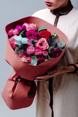 Bouquet of flowers in terracotta foamiran package in the hands of a woman florist. Rose, carnation, eryngium, eucalyptus, celosia.の写真素材
