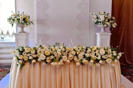 Wedding presidium in restaurant, free space. Wedding banquet table for newlyweds with flowers, greenery, peach cloth. Lush floral arrangement on wedding table. Luxury wedding decorationsの写真素材
