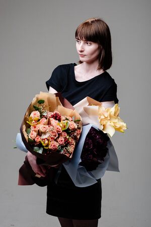 Portrait of young female florist brown-haired with a haircut with bouquets of flowersの写真素材