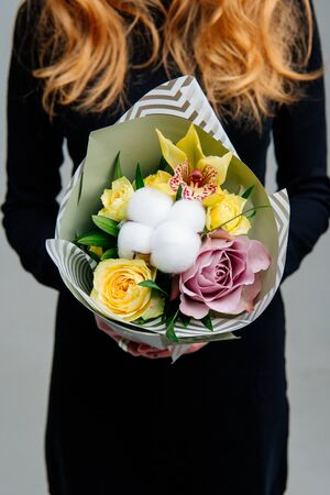 Bouquet of flowers in pistachio package in the hands of red-haired girl florist on light background. Rose, cottonwood box, orchid.の写真素材