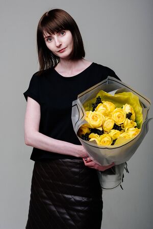 Portrait of young female florist with bouquet of flowers in transparent package in the hands. Rosa spray Catalina, rhamnusの写真素材
