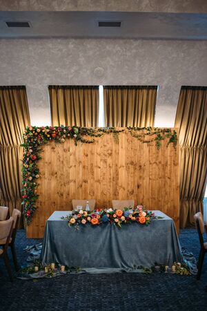 Wedding presidium in restaurant, free space. Wedding banquet table for newlyweds with flowers, greenery, blue velvet and candles . Lush floral arrangement on wedding tableの写真素材