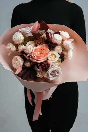 Bouquet of flowers in peach foamiran package in the hands of a woman florist on a light background. Rosa, cotinus, brunia, lagurus.の写真素材