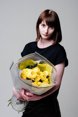 Portrait of young female florist with bouquet of flowers in transparent package in the hands. Rosa spray Catalina, rhamnusの写真素材