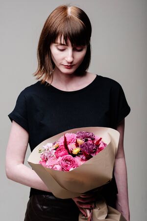 Portrait of young female florist with bouquet of flowers in beige package in the hands. Rosa spray, dahlia, celosia, matthiola, carnation.の写真素材