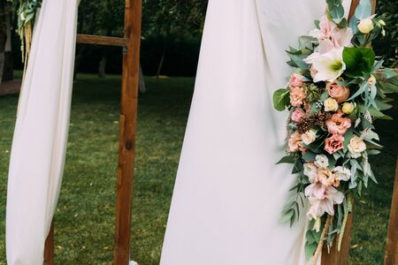 Fragment of wooden arch for the wedding ceremony, decorated cloth, flowers and greeneryの写真素材