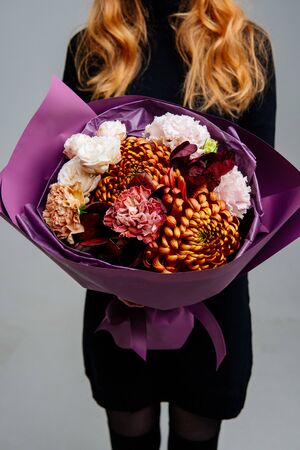Bouquet of flowers in purple package in the hands of red-haired girl florist on light background. Rose, chrysanthemum, carnation, cotinus.の写真素材