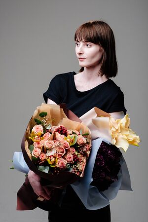 Portrait of young female florist brown-haired with a haircut with bouquets of flowersの写真素材